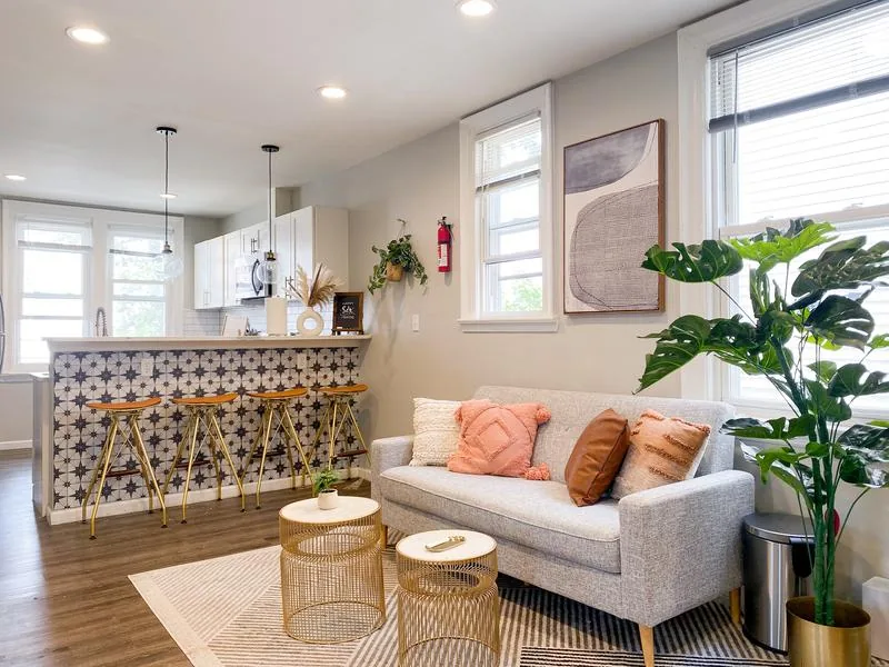 Open living + kitchen — gray sofa, terracotta pillows, star-tile bar with gold + orange barstools