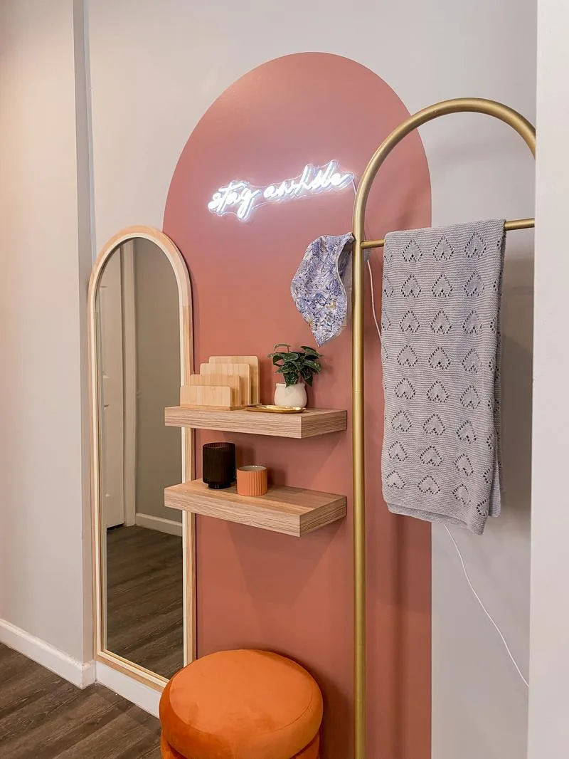 "Stay Awhile" neon on rose arch — arched mirror, gold rack, orange velvet ottoman